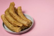 Delicious Spanish churros in plate on pink backdrop — Stock Photo