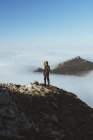 Voyageur debout sur le bord rocheux avec fond de pic de montagne dans les nuages . — Photo de stock