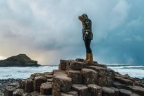 Vue latérale de la femme touristique debout sur des pierres au bord de la mer par temps nuageux . — Photo de stock