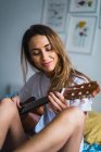 Mulher sorridente tocando guitarra na cama em casa — Fotografia de Stock