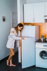 Vista lateral da mulher em pé na geladeira aberta na cozinha em casa
. — Fotografia de Stock