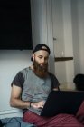 Бородатий чоловік сидить на підлозі і використовує ноутбук вдома — стокове фото