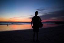 Silhouette einer Person mit Rucksack, die in der Abenddämmerung an der Küste steht. — Stockfoto