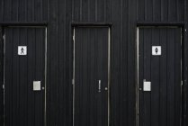 Vista exterior de fachada con puertas de color negro a baños masculinos y femeninos . - foto de stock