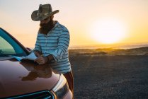 Selbstbewusster Reisender liest Landkarte auf Motorhaube am Strand — Stockfoto