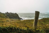 Blick auf Zaun und grüne Küstenfelsen am Meeresufer — Stockfoto