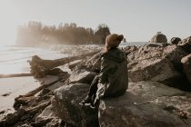 Vista trasera del turista sentado en rocas costeras en vista admiradora - foto de stock