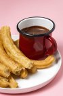 Typical Spanish churros with hot chocolate sauce in cup on pink — Stock Photo