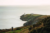 Distant view of tourist standing on rocky coast covered with grass. — Stock Photo