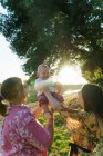 Вид ззаду лесбійської пари, що грає з дитиною на заході сонця — стокове фото