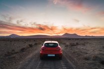 Rear view of red car parked on rural road leading to mountains in evening — Stock Photo