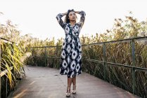 Жінка в красивій сукні позує з піднятими руками і дивиться в сторону паркового мосту — стокове фото