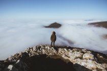 Rear view of man on rocky cliff against scenic cloudscape — Stock Photo