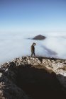 Man on walking rocky cliff in clouds against mountain peak in fog — Stock Photo