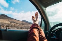 Colheita pés masculinos saindo da janela do carro no fundo do vale da montanha à luz do sol . — Fotografia de Stock