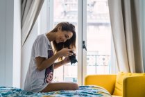 Side view of smiling woman sitting on bed and looking shots on camera — Stock Photo