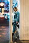 Side view of woman in denim jacket leaning on wall on night street scene — Stock Photo