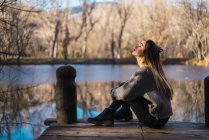 Side view of woman sitting on pier above autumnal pond — Stock Photo