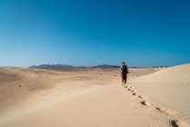 Back view of man with backpack exploring endless sandy terrains in sunlight. — Stock Photo