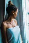 Портрет молодой женщины в полотенце, смотрящей в окно — стоковое фото