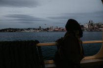 Vista trasera de la mujer de pie en el suelo del ferry y admirar paisaje urbano - foto de stock