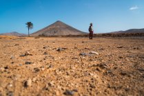 Vue lointaine de l'homme avec sac à dos marchant dans le désert tropical — Photo de stock
