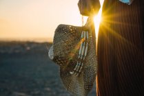 Crop shot of male holding cowboy straw hat and standing in sunset sunlight on shoreline. — Stock Photo