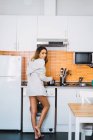 Jeune femme cuisine sur la cuisine et regardant par-dessus l'épaule à la caméra — Photo de stock