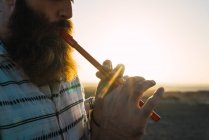 Снимок бородатого человека, играющего на трубе на фоне солнечного берега . — стоковое фото