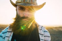 Ritratto di uomo barbuto in cappello contro la luce del sole — Foto stock