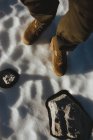 Olhando para baixo vista do viajante em botas de inverno em pé na superfície nevada com pedras . — Fotografia de Stock
