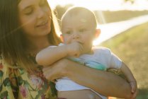 Cosecha madre sosteniendo niño en las manos en parque - foto de stock