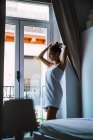 Vista lateral da mulher posando em toalha por janela em casa — Fotografia de Stock