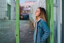 Side view of young woman leaning on fence at street scene — Stock Photo