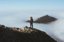 L'uomo sulla scogliera rocciosa contro la cima della montagna guardando fuori dalle nuvole — Foto stock