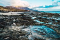 Landscape of ocean coastline with dirty rough formations on background of sky and mountains. — Stock Photo