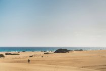 Далекий взгляд на человека, идущего по песчаным дюнам на берегу — стоковое фото