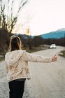 Rear view of woman hitchhiking on rural road — Stock Photo