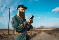 Vista lateral do homem que navega smartphone na estrada rural — Fotografia de Stock