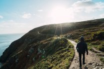 Вид сзади туриста, идущего по холму в солнечный день — стоковое фото