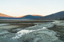 Landscape view of gray land with shallow water on background of mountains. — Stock Photo
