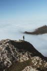 Distant view of man on rocky cliff in clouds — Stock Photo