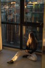 Mulher loira sentada no chão perto da janela e olhando para longe — Fotografia de Stock