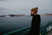 Vista lateral del hombre barbudo de pie en ferry flotando en el océano . - foto de stock