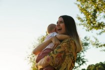 Fröhliche Mutter umarmt Kind im Park — Stockfoto