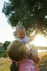 Retrato de criança em mãos de mãe no parque de verão no pôr do sol — Fotografia de Stock