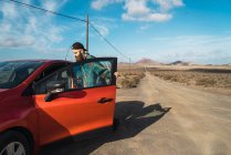 Вид сбоку: боковой турист садится в красный автомобиль на сельской дороге — стоковое фото
