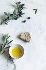 Directly from above view of olive oil in bowl and olive branches with bread on white background — Stock Photo