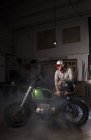 Профессиональный механик, опирающийся на собственный мотоцикл в мастерской — стоковое фото
