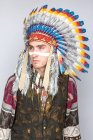 Молодой человек с чертой на лице позирует в традиционном индейском костюме — стоковое фото